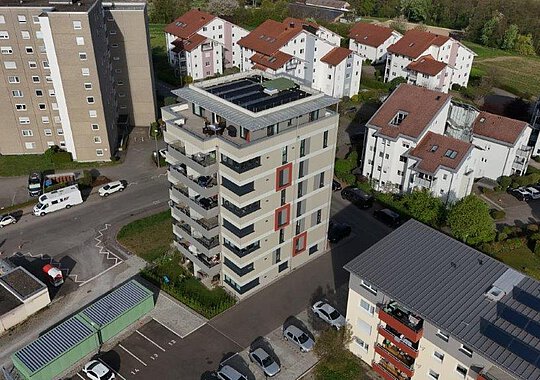 Luftaufnahme eines neu gestalteten Hochhauses mit markanten roten Fensterrahmen, Balkonen und Solarpanels, eingebettet in ein Wohngebiet in Tettnang.