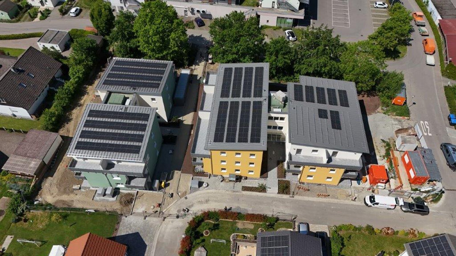 Luftbild von mehreren Neubauten mit gelber und grüner Fassade in Salem, alle mit großflächigen Solaranlagen auf den Dächern, umgeben von Straßen und Bäumen.