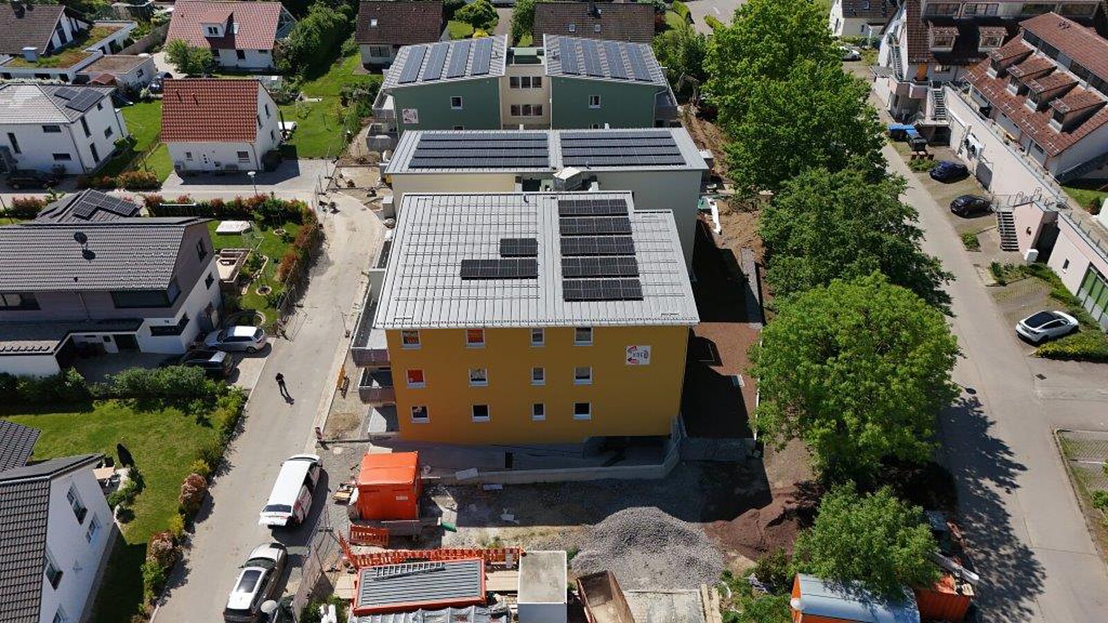 Luftbild von mehreren Neubauten mit gelber und grüner Fassade in Salem, alle mit großflächigen Solaranlagen auf den Dächern, umgeben von Straßen und Bäumen.