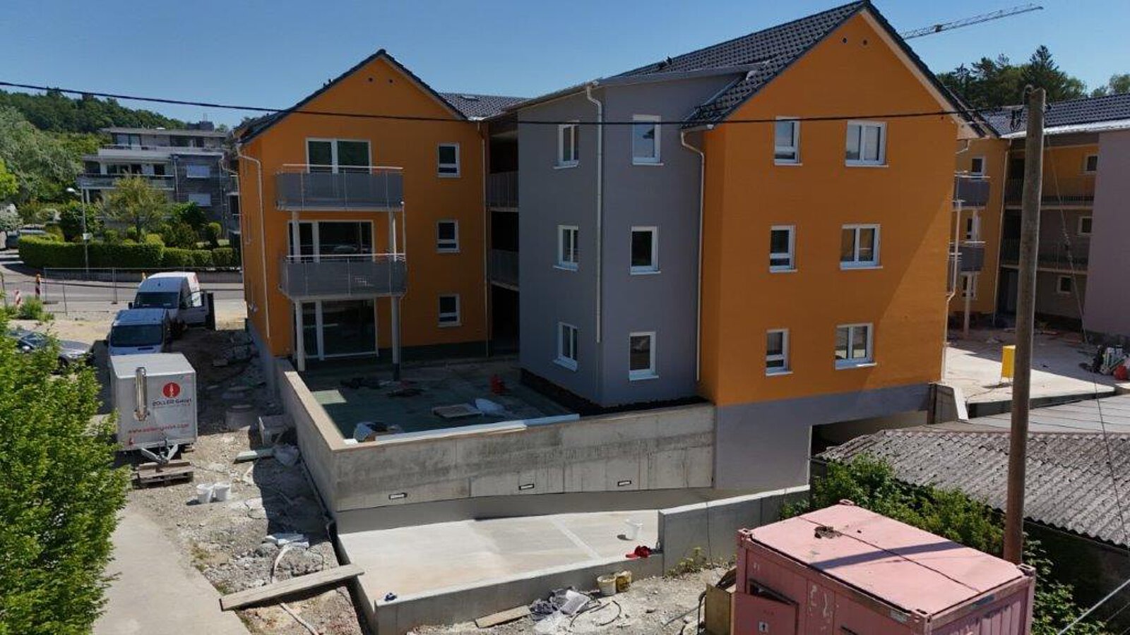 Luftaufnahme eines Wohngebäudes mit Innenhof und Balkonen, teilweise im Rohbauzustand, umgeben von angrenzenden Gebäuden und Baustelleninfrastruktur.