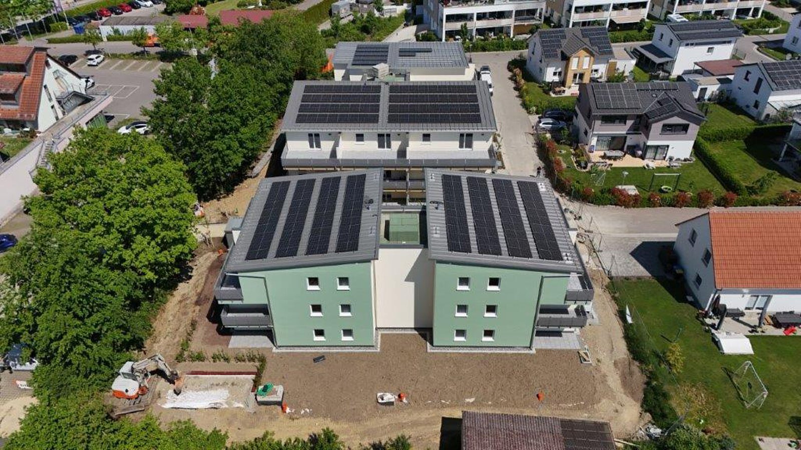 Luftbild von mehreren Neubauten mit gelber und grüner Fassade in Salem, alle mit großflächigen Solaranlagen auf den Dächern, umgeben von Straßen und Bäumen.